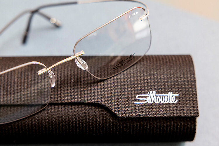 Randlose Brille von Silhouette liegt auf einem schwarzen Etui mit Markenlogo, präsentiert auf hellem Untergrund.
